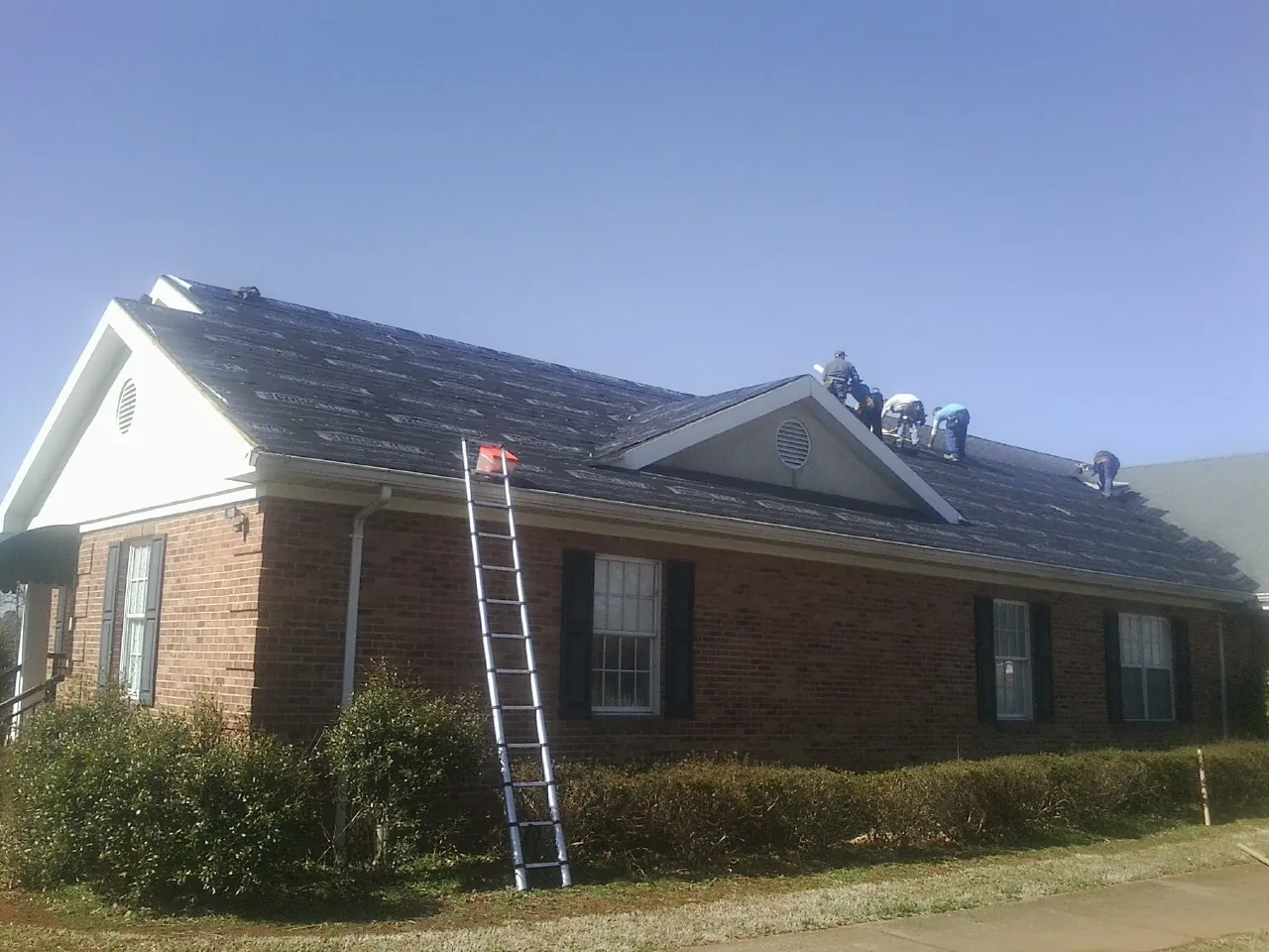Crew tearing shingles off a brick ranch roof with a ladder set — Metal Roof Repair work by our crew in Dorchester