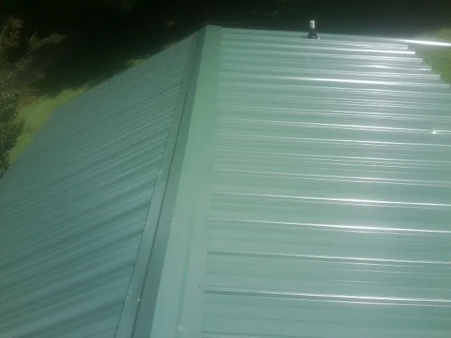 New green metal panels meeting at the ridge of a roof — Flat Roof Repair work by our crew in Dorchester